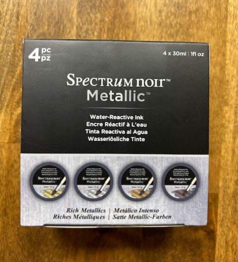 An image of a product box for a four-pack of Spectrum Noir Metallic Water-Reactive Inks in the Rich Metallics color set. These inks are water-reactive and offer a rich, opaque layer of color with a pearlescent, metallic finish. 