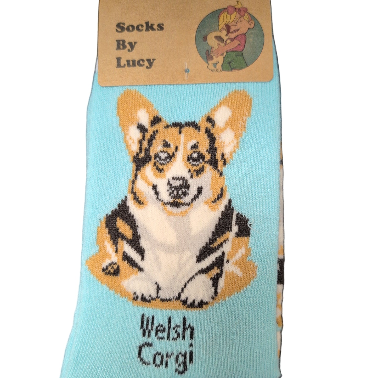 Sock with a Welsh Corgi design on a cardboard holder labeled 'Socks By Lucy' on a dark surface.