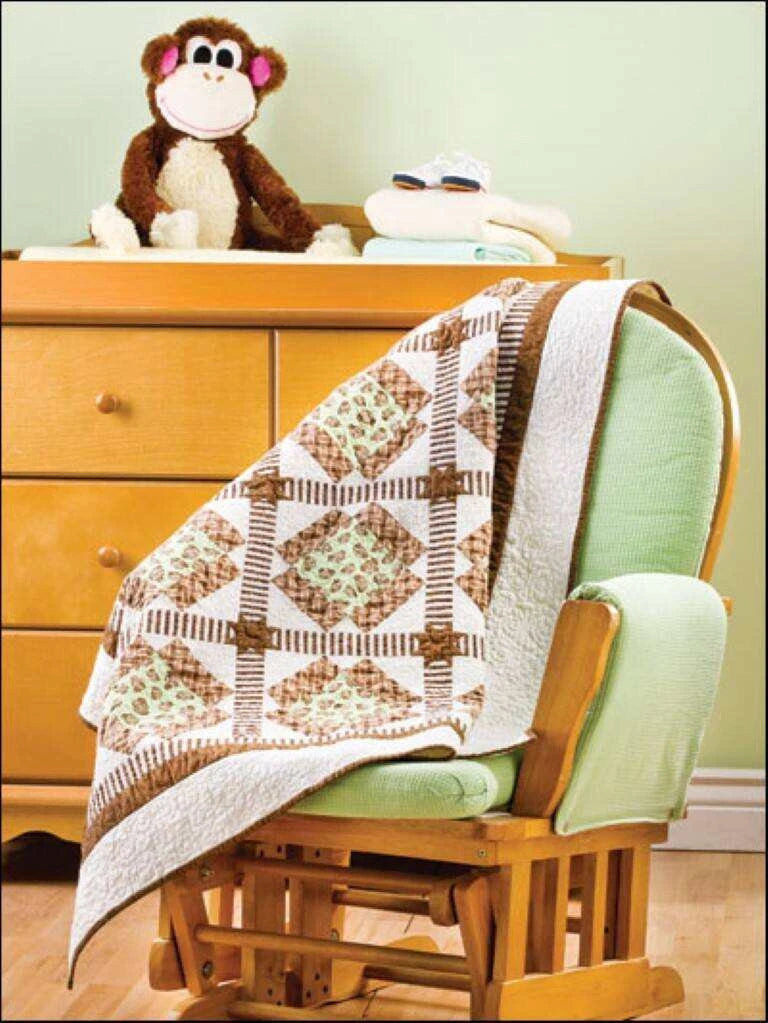 Quilt draped over a rocking chair with a monkey toy on a dresser in the background.