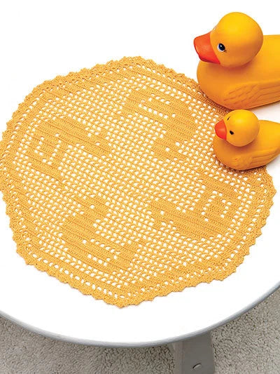 Yellow doily with a duck design on a white surface, featuring two yellow rubber ducks.