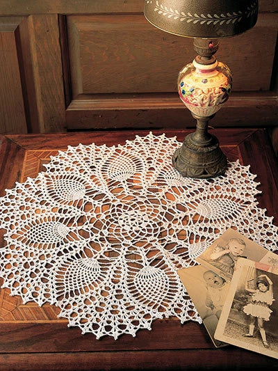 White crocheted doily on a wooden surface with a vintage lamp and photos in the background.