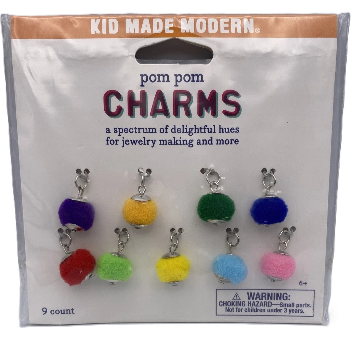 Packaged pom pom charms with colorful beads and metal clasps on a white background.