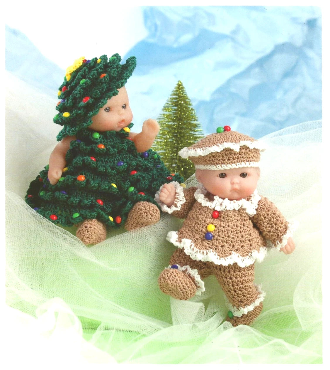 Two small dolls dressed in festive outfits with a Christmas tree and gingerbread man theme.