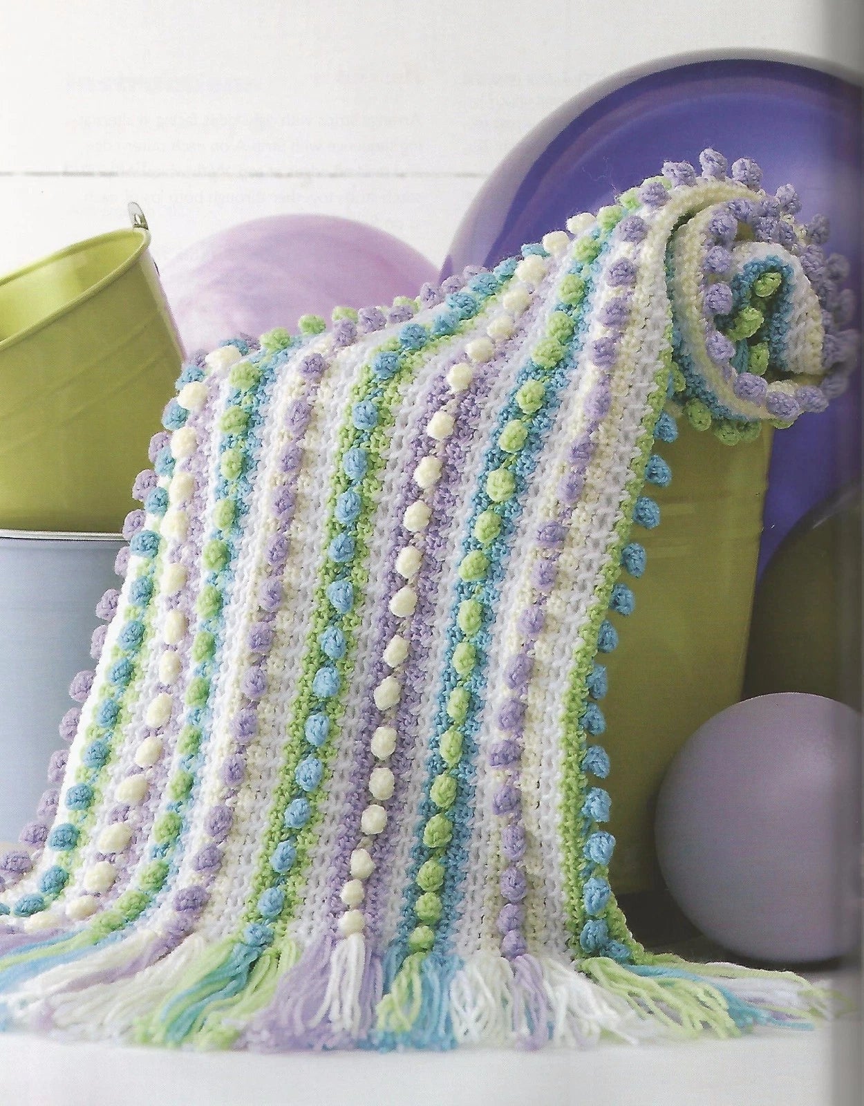 Colorful knitted blanket with pom-pom trim draped over a chair.