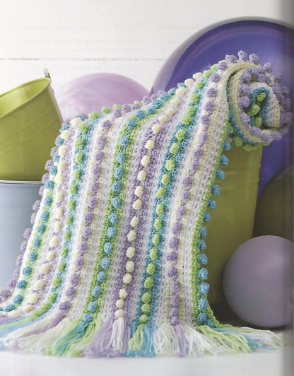 Colorful knitted blanket with pom-pom trim draped over a chair.