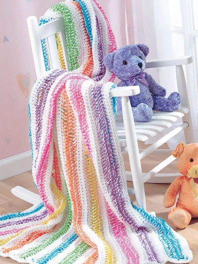 Colorful knitted blanket draped over a white chair with two teddy bears in a room.