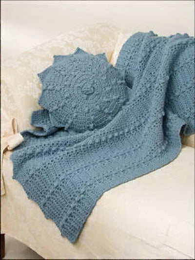 Blue knitted blanket draped over a chair with a matching pillow.