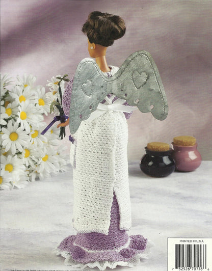 Knitted angel doll with wings and a purple dress, surrounded by flowers and jars on a textured surface.