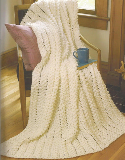 Knitted blanket draped over a chair with a cup and pillow in a cozy room.