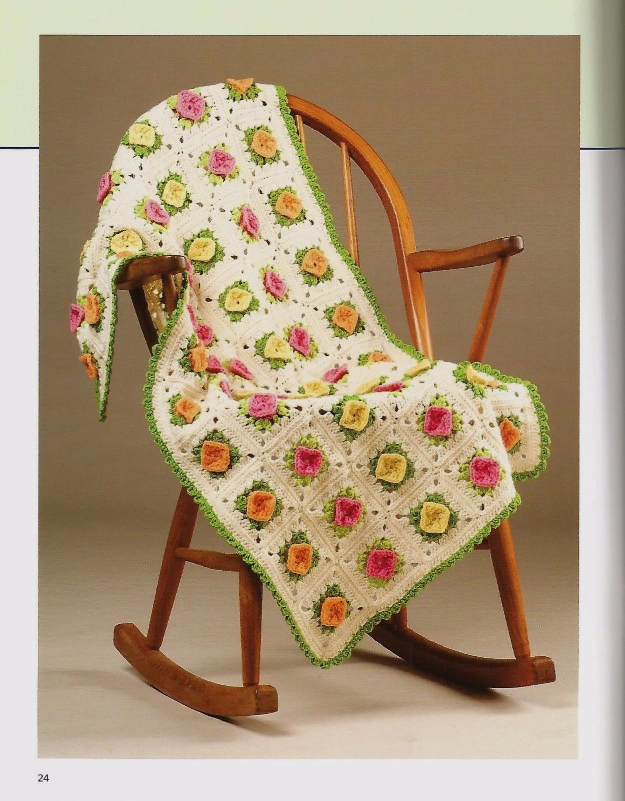 Crocheted blanket with floral pattern draped over a wooden rocking chair on a beige background