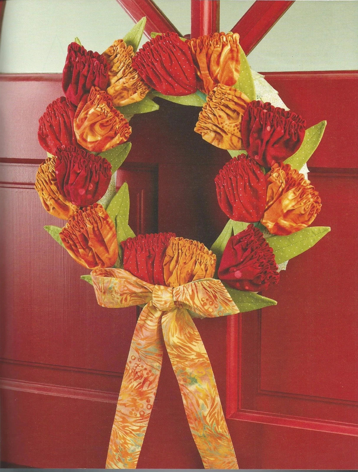 Decorative wreath with red and orange flowers and a bow on a red door.