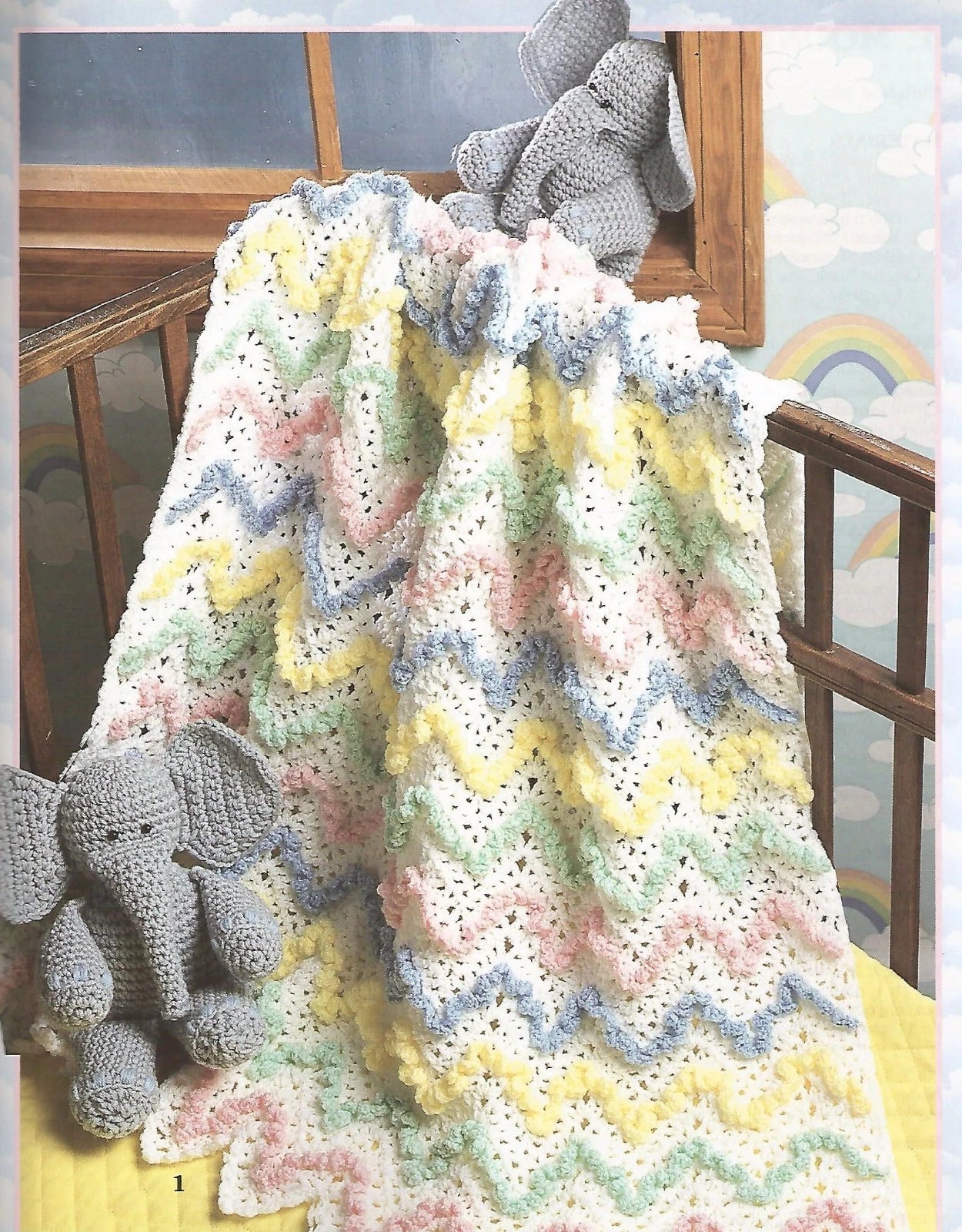 Crocheted baby blanket with colorful patterns draped over a crib, accompanied by a gray elephant toy.