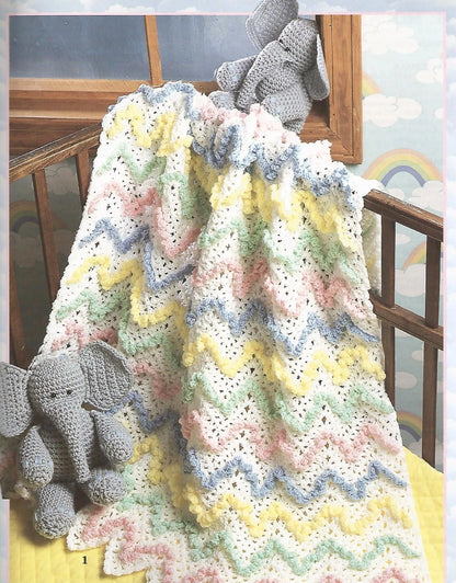 Crocheted baby blanket with colorful patterns draped over a crib, accompanied by a gray elephant toy.