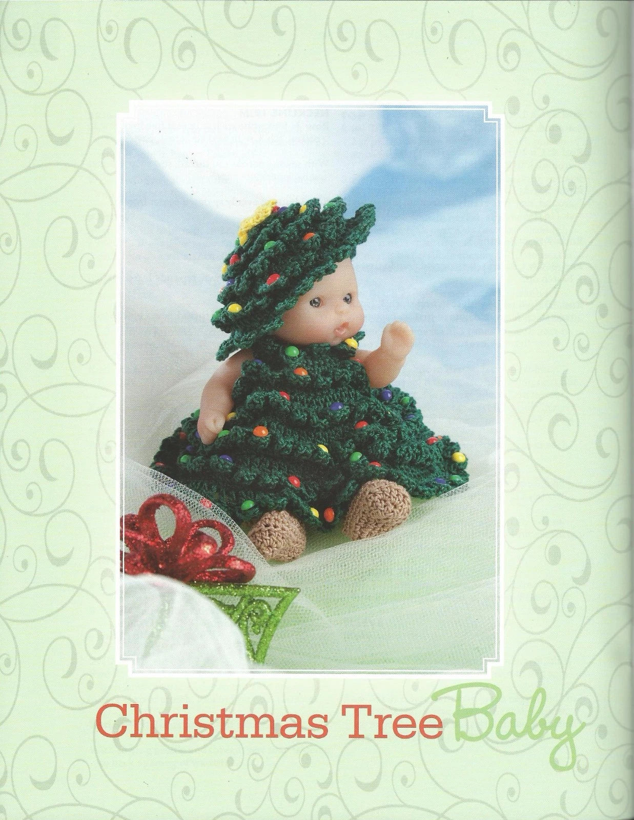 Baby doll in a Christmas tree costume on a decorative card with a green border.