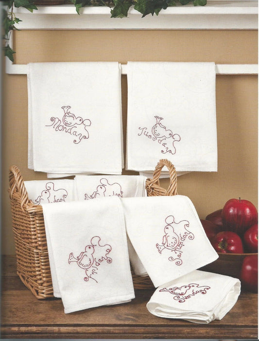 Set of white towels with embroidered designs in a basket on a wooden surface.