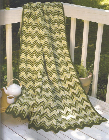 Knitted green and white blanket on a wooden railing with a teapot and cup in the background.