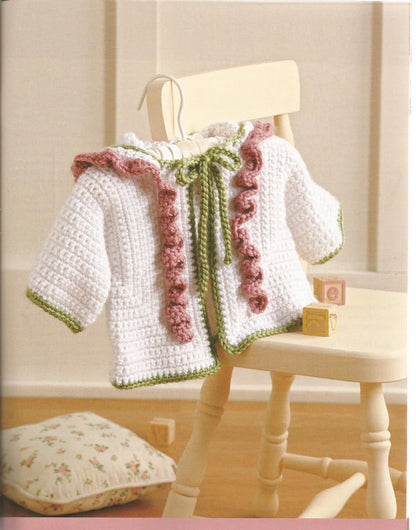 White crocheted baby jacket with pink and green accents on a mannequin against a light background.