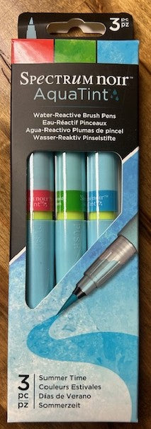 A three-pack of Spectrum Noir AquaTint water-reactive brush pens in the 'Summer Time' color set is displayed. The pens are filled with bright water-soluble dye-based ink and dispensed through a fine nylon brush. 